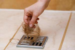 Woman removing hair clump from the shower drain photo