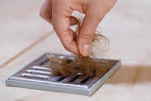 mujer quitando mechones de pelo del desagüe de la ducha foto