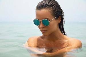 Beautiful woman is bathing in the sea wearing sunglasses photo