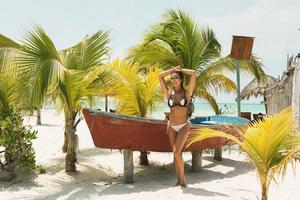 Beautiful woman wearing bikini and sunglasses beside a old boat photo