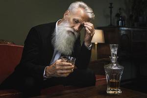 Handsome and bearded senior man drinking whiskey photo