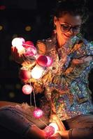 Happy woman wearing glowing jacket with sequins is holding light balls in her hands photo