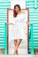 Cute woman wearing beautiful white dress is posing near colorful wooden house photo