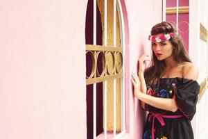 bella mujer con vestido tradicional mexicano posa junto a una pared rosa foto