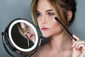 Beautiful woman with make-up brush and round mirror with LED light photo