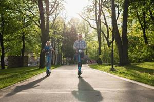 madre e hija montando scooters eléctricos en el parque de la ciudad foto