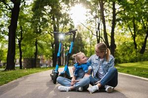 madre e hija sentadas en una carretera después de un paseo en scooters eléctricos foto