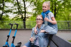 madre e hija con scooters eléctricos están bebiendo limonada en el parque de la ciudad foto
