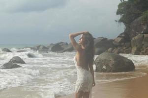 Young woman wearing beautiful white dress is posing on the beach photo