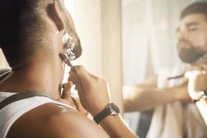 Man looking in the mirror and shaving his beard with a straight razor