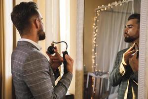 Handsome bearded man is using atomizer nozzle with perfume photo