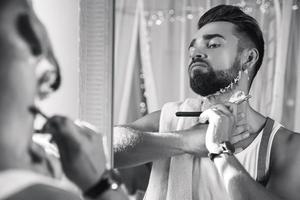 hombre mirándose en el espejo y afeitándose la barba con una navaja de afeitar foto
