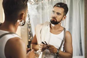 Man looking in the mirror, smoking a cigarette and shaving his beard with a straight razor photo