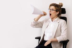 Motivated businesswoman shouting into the sheet of paper rolled like a loud speaker photo