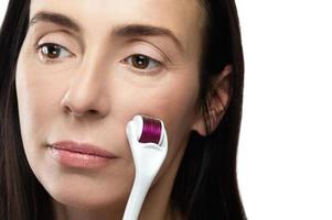 Middle aged woman using mesoroller for her facial skin. photo