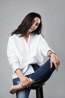bella modelo de moda de mediana edad con camisa blanca y jeans en un estudio fotográfico foto