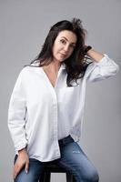 bella modelo de moda de mediana edad con camisa blanca y jeans en un estudio fotográfico foto