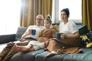 Family relaxing on a the sofa and  drinking hot tea in the living room of their cozy apartment photo