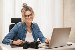 mujer feliz fotógrafa con una cámara sin espejo en el lugar de trabajo foto