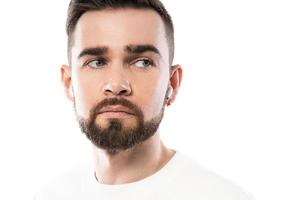 Handsome bearded man in white clothes  using wireless earbuds on white background photo