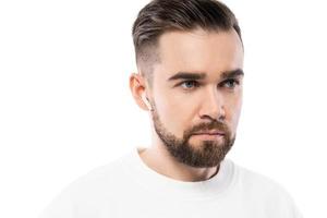 hombre guapo con barba vestido de blanco usando auriculares inalámbricos con fondo blanco foto