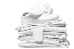 Stack of white clothes, trainers and baseball cap with a blank garment tag on white background photo