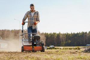 Man using aerator machine to scarification and aeration of lawn or meadow photo