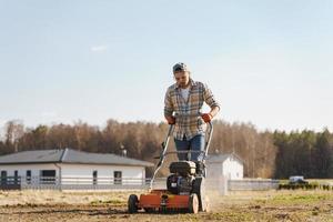 Man using aerator machine to scarification and aeration of lawn or meadow photo