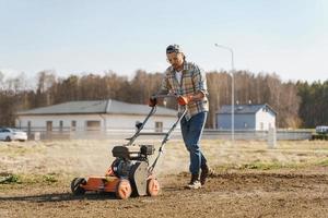 Man using aerator machine to scarification and aeration of lawn or meadow photo