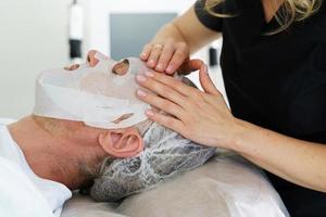 cosmetóloga aplicando máscara de hoja en la cara del cliente foto