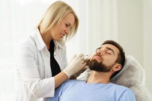 Female doctor and male client during filler injections in clinic photo