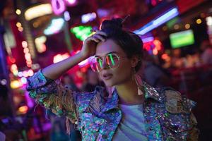mujer elegante con chaqueta con lentejuelas brillantes en la calle de la ciudad con luces de neón foto