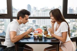 Happy couple eating healthy breakfast in modern apartment with large windows and city view photo