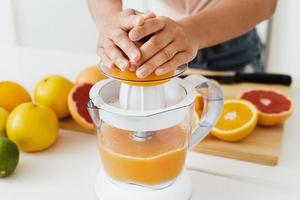 manos femeninas y exprimidor de cítricos durante la preparación de jugo de naranja fresco foto