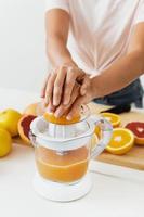 manos femeninas y exprimidor de cítricos durante la preparación de jugo de naranja fresco foto