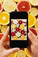 Female hands with smartphone taking photos of different citrus fruits