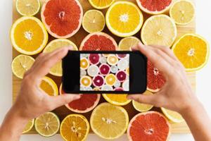 Female hands with smartphone taking photos of different citrus fruits