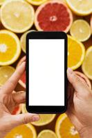 Female hand holding smartphone with empty screen for your design against citrus fruits background photo