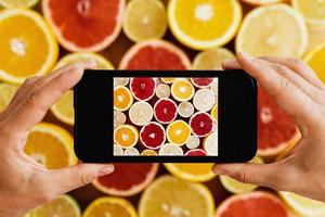 Female hands with smartphone taking photos of different citrus fruits