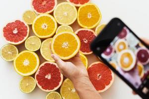 Female hands with smartphone taking photos of different citrus fruits