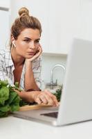 Young pretty woman using laptop for online recipe search to cook at home photo