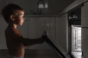 un niño curioso abre el horno caliente. concepto de seguridad y posibles problemas con niños desatendidos.