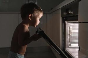 Curious baby boy opens the hot oven. Concept of safety and possible problems with unattended children. photo