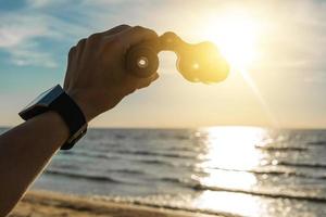 Adventure - Female hand with a vintage binocular against bright sun light on beautiful beach with nice blue sky. photo