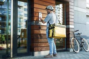 Express food delivery courier with insulated bag using intercom. photo