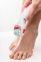 Female feet and electric foot scrubber or massage device on white background photo