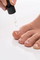 Closeup of female foot and bottle of nourishing cuticle oil with dropper photo