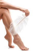 Female feet with smooth skin and soft ostrich feather on white background photo