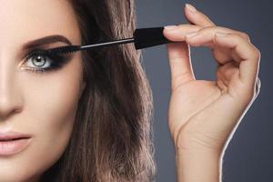 Woman with beautiful make-up is applying mascara on her lashes photo