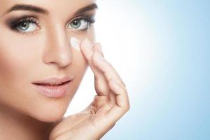 Beautiful woman applying moisturizing cream under her eye photo